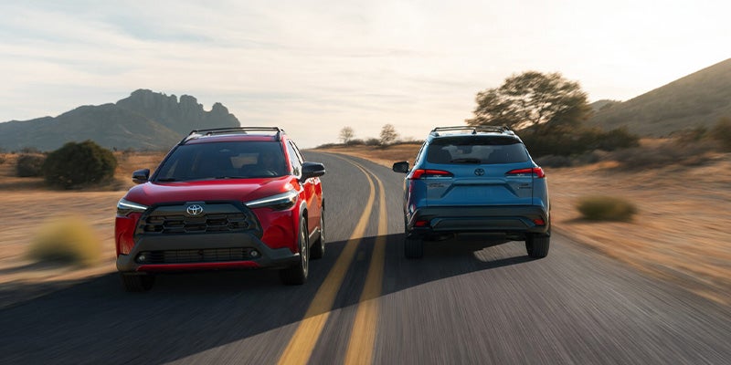 Red and blue Toyota SUVs driving on a winding desert road with mountains in the background