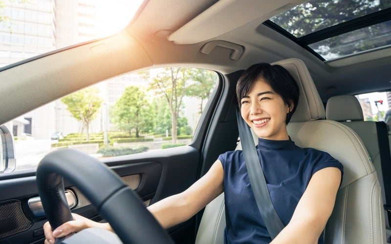 A person driving a modern car, holding the steering wheel, with sunlight streaming through the sunroof