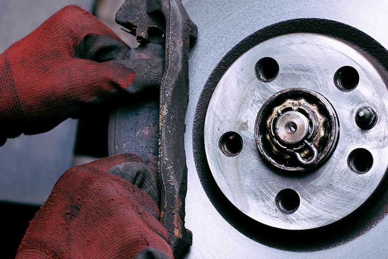 Gloved hands adjusting a rusty brake caliper next to a clean, silvery-grey brake disc