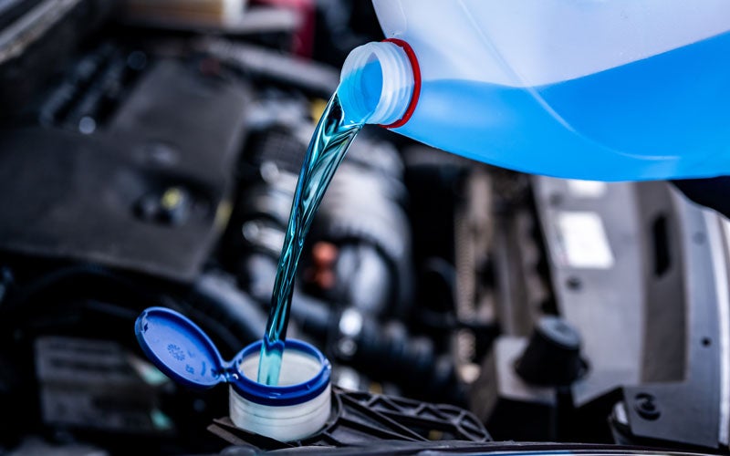 close-up view of a car engine compartment where a liquid is being poured into a reservoir