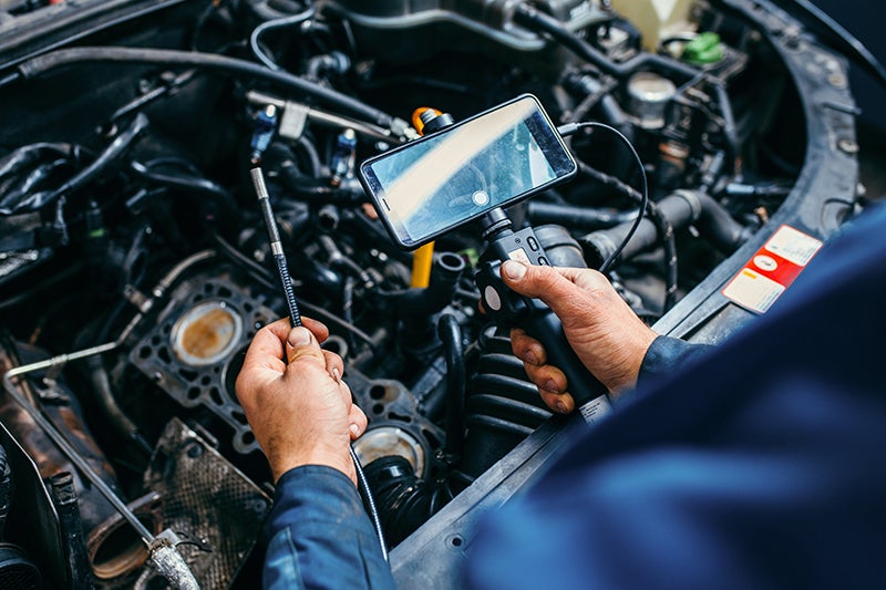 Mechanic using a borescope camera with a smartphone display to inspect the intricate details of a car engine